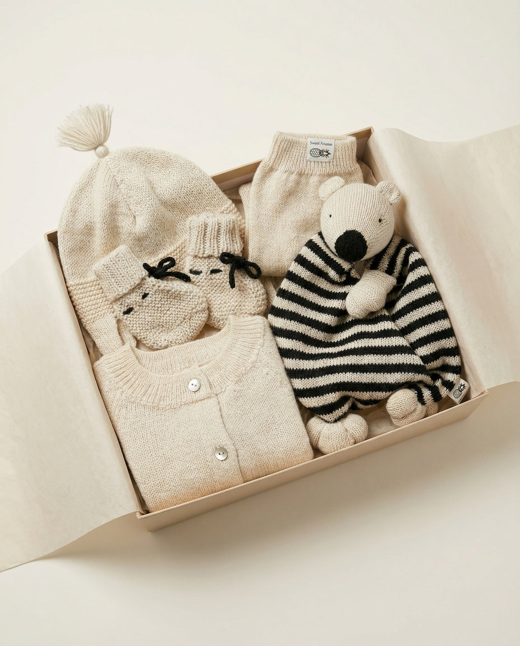 Baby clothing set with hat, sweater, and toy in a box on a light background