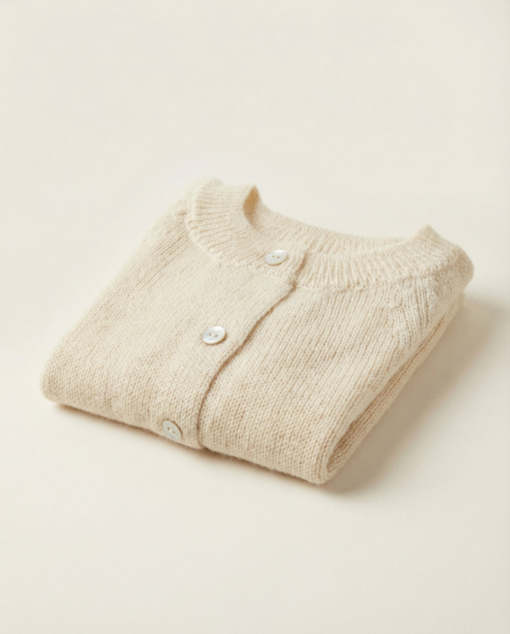 Folded beige baby cardigan on a light beige background