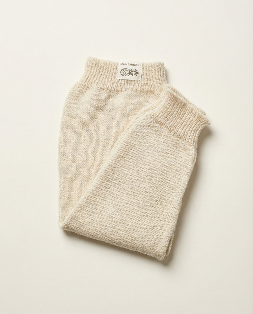 Folded beige knitted baby pants on a light beige background