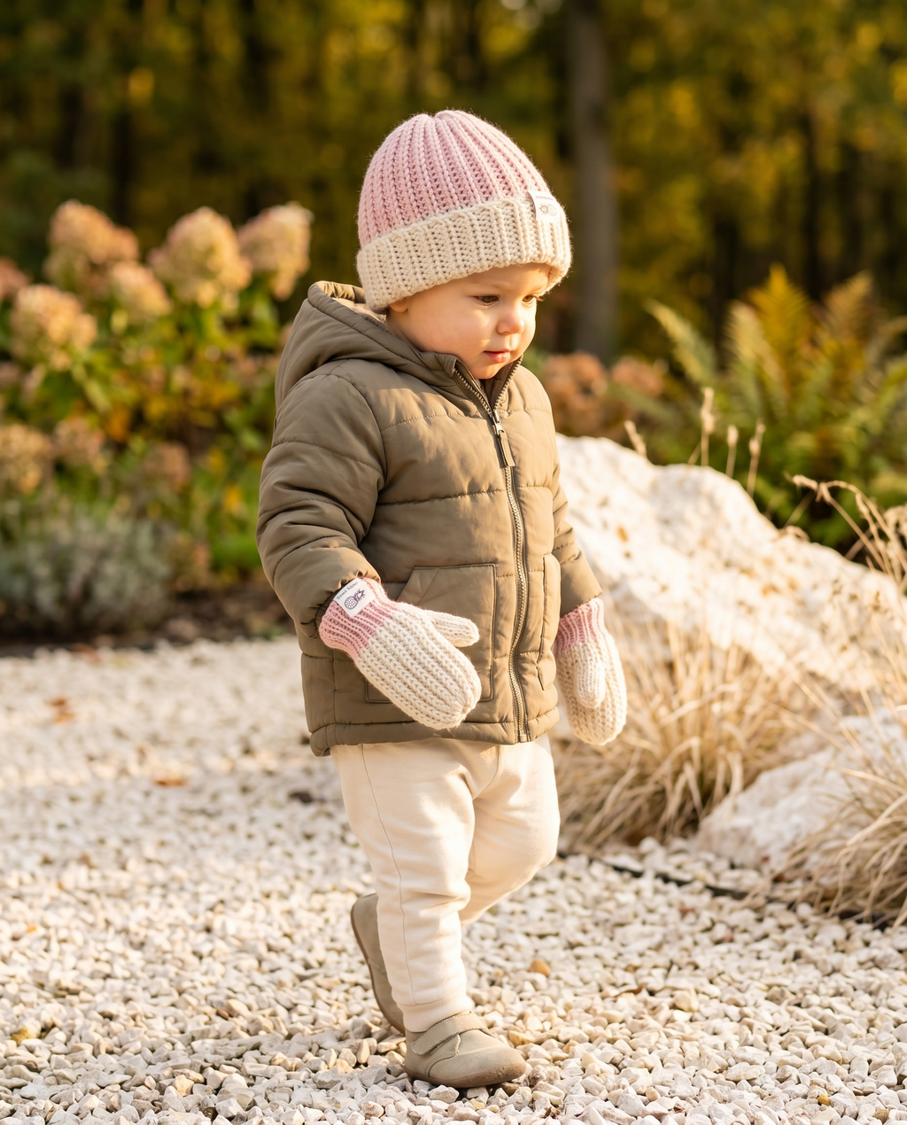 Child in winter clothing standing on a gravel path with plants in the background