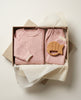 Pink baby outfit with a wooden teether in a box on a light background